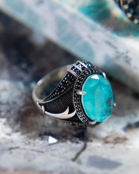 Silver men's ring with a large blue gemstone and black stones lying on a stone surface is sparkling
