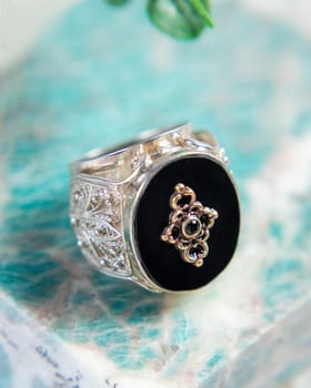 Silver ring with black onyx cabochon and floral ornaments on turquoise stone background