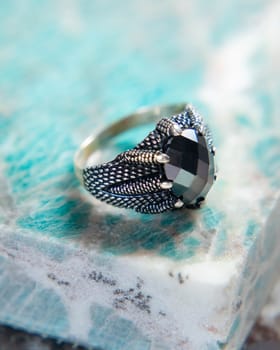 Silver ring with black gemstone and claw design resting on amazonite stone