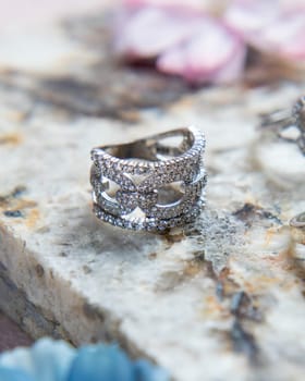 Silver ring with diamonds on stone surface with flowers out of focus in the background