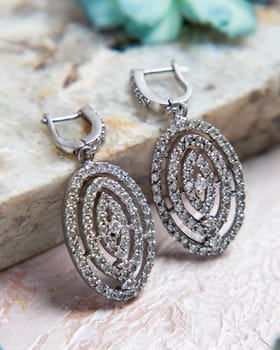Pair of oval diamond earrings with a french lock closure lying on a stone surface
