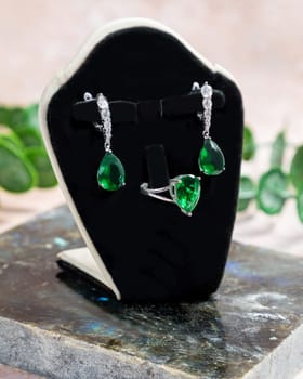 Elegant silver emerald jewelry set with earrings and a ring standing on a black display