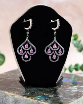 Silver earrings with pink gemstones are displayed on a black jewelry display stand