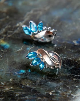 Pair of silver earrings with blue topaz lying on dark stone surface
