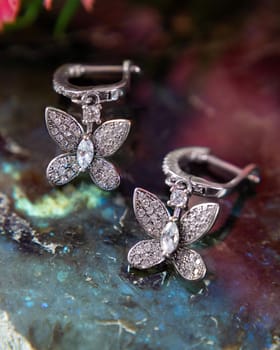 Luxurious earrings with sparkling butterfly shaped pendants reflecting in the surface of a colorful gemstone