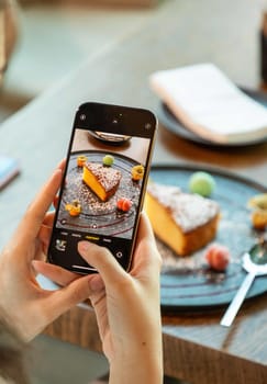 Woman using smartphone taking photo of delicious cake on plate in restaurant