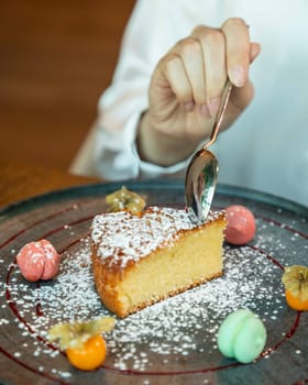 Woman is enjoying a delicious piece of cake decorated with powdered sugar and fruit