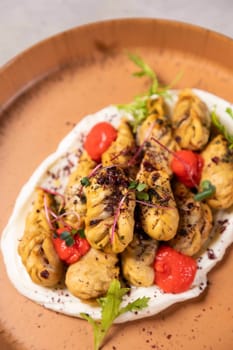 Fried dumplings laying on a white sauce are being served on a plate and garnished with microgreens