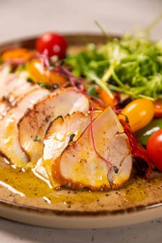 Sliced grilled chicken breast is served on a plate with fresh salad and mustard sauce