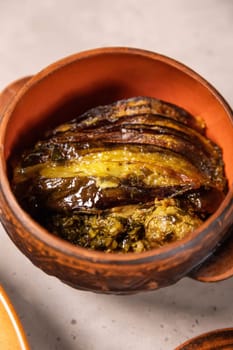 Oven baked eggplant slices lying on top of herbs and spices, served in traditional clay pot