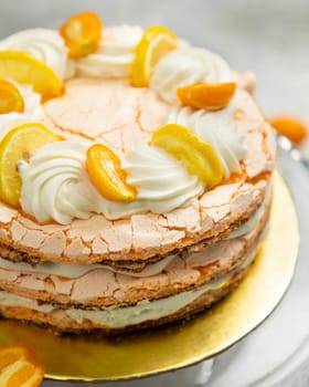 Layered meringue cake topped with lemon and kumquat slices and whipped cream swirls is waiting to be eaten
