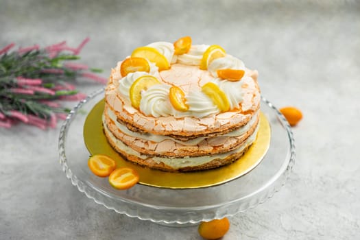 Delicious meringue cake decorated with slices of lemon and kumquat, standing on glass plate, on gray background