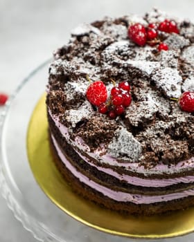 Layered chocolate cake with chocolate crumble topping, decorated with berries and icing sugar, sitting on a glass plate