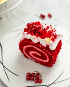 Red velvet swiss roll cake lying on white plate decorated with redcurrant, cream and gold leaf