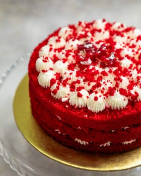 Red velvet cake with cream cheese frosting decorated with red currant berries standing on a golden cake board