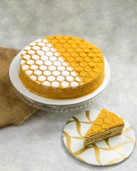 Delicious homemade honey cake decorated with honeycomb pattern standing on cake stand with slice of cake on plate
