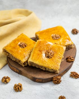Squares of baklava, a sweet dessert pastry, are arranged on a wooden board, ready to be enjoyed