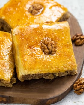 Squares of baklava topped with walnuts are resting on a wooden board
