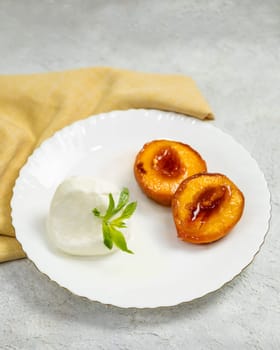 Delicious grilled peach dessert with ice cream and mint on white plate is served on the table