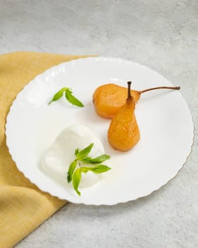 Two caramelized pears with a scoop of vanilla ice cream and mint on a white plate