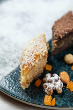 Delicious baklava piece covered in coconut flakes laying on a plate with candied orange peels and a variety of nuts