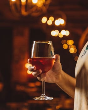 Man holding a glass of red wine with a blurred background of warm lights