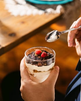 Businessman holding a glass of tiramisu topped with raspberries and cocoa powder, with a spoon hovering above
