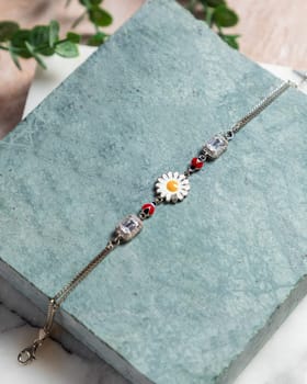 Silver bracelet with a daisy flower and red enamel detail is laying on a stone
