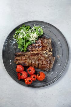 Delicious t-bone steak with grilled cherry tomatoes and arugula salad on a gray plate