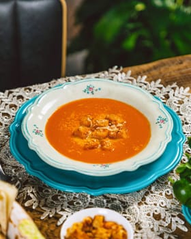 Creamy tomato soup with croutons and grated cheese served on a vintage table with a rustic tablecloth