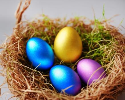A nest of eggs with blue, yellow, and purple eggs. The nest is made of straw and the eggs are shiny