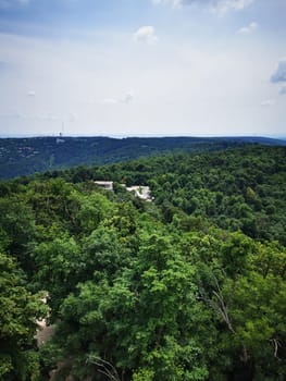 A stunning view captures rolling green hills dotted with trees, with distant mountains visible under a bright blue sky, showcasing the tranquility of nature.
