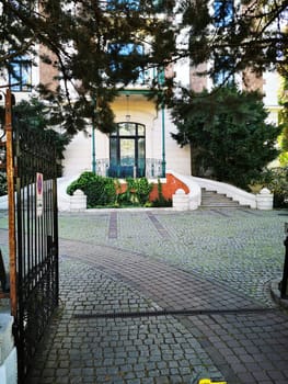 The entrance features intricate architecture with a well-maintained path, vibrant greenery, and inviting surroundings, creating a peaceful atmosphere for visitors.