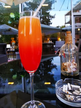 A tall glass filled with a colorful cocktail showcases a vibrant gradient of orange and red. The setting features contemporary lounge furniture and a relaxing atmosphere.