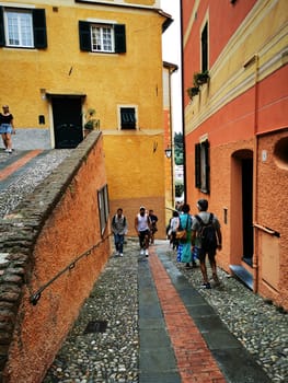 A vibrant cobblestone street lined with orange and yellow buildings invites travelers. Groups explore the winding path, soaking in the charming architecture and atmosphere.