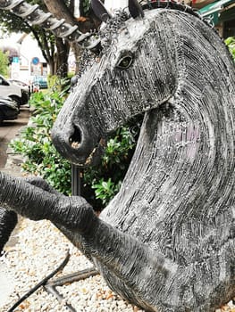 A striking metal unicorn sculpture stands proudly in a vibrant urban area, surrounded by lush foliage and parked cars, showcasing intricate details in its design.