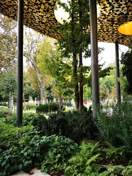 Visitors enjoy a serene urban park filled with vibrant plants and trees, while unique overhead lights create a distinctive ambiance above the greenery.