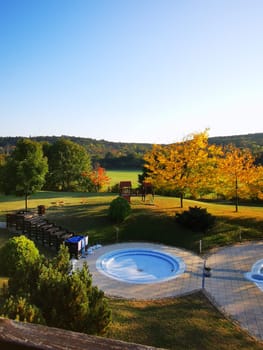 A serene outdoor landscape showcases two inviting hot tubs surrounded by vibrant autumn foliage under a clear blue sky. Perfect for relaxation.