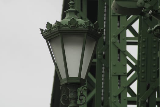 An ornate green street lamp stands prominently, showcasing intricate designs while framed by a stark industrial structure, highlighting urban architecture.