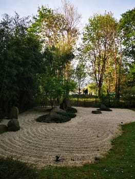 A serene Japanese zen garden showcases raked gravel patterns surrounded by stones and greenery, inviting peaceful contemplation during sunset in the city park.