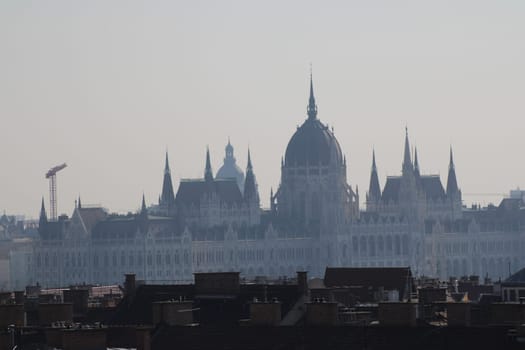 The Parliament building in Budapest stands majestically, partially hidden by morning mist, highlighting its intricate architecture and historical significance in the city.