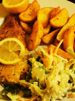 A delicious plate features crispy fried fish adorned with lemon slices, accompanied by flavorful potato wedges and a refreshing coleslaw, perfect for lunch or dinner.