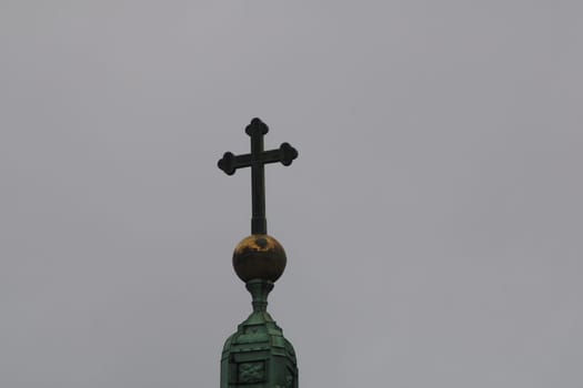 A cross is prominently featured on top of a church spire, with a grey sky providing a dramatic backdrop. The structure symbolizes faith and architectural elegance.