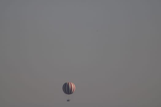 A vibrant hot air balloon ascends gracefully into the clear skies at dawn, casting a calm silhouette against the pastel colors of the horizon.