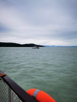 A small boat glides through the tranquil waters, approaching an island surrounded by gentle waves and a backdrop of overcast skies in the afternoon light.