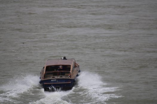 A speedboat plows through rough waters, producing splashes as it moves swiftly. The overcast sky adds a dramatic backdrop to this exciting maritime scene.