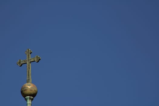 The view captures a tall cross atop a dome set against a bright blue sky, representing faith and tranquility. The scene evokes a sense of peace and devotion.