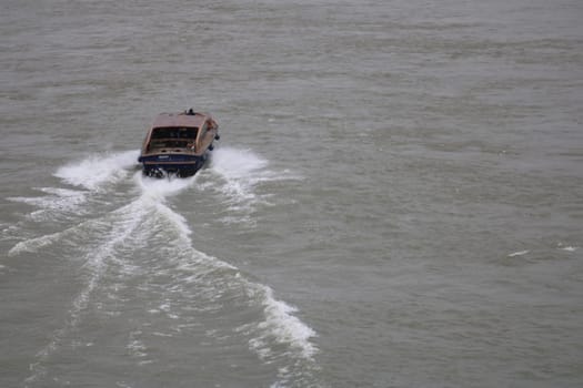 A small boat navigates through tranquil waters under a cloudy sky, leaving behind a series of soft ripples and trails in its wake, showcasing a peaceful journey.