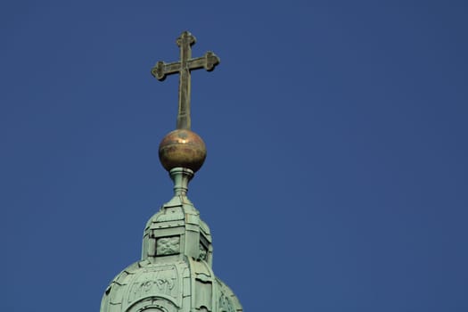 The steeple features an ornate cross sitting on a golden orb, beautifully contrasting with the clear blue sky overhead, showcasing architectural elegance.