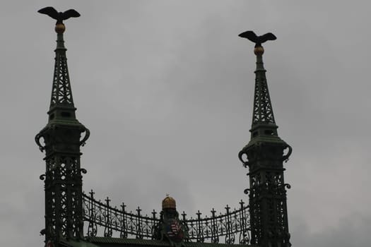Two intricately designed spires topped with eagle sculptures rise above the structure, set against a dramatic cloudy backdrop, showcasing architectural beauty.